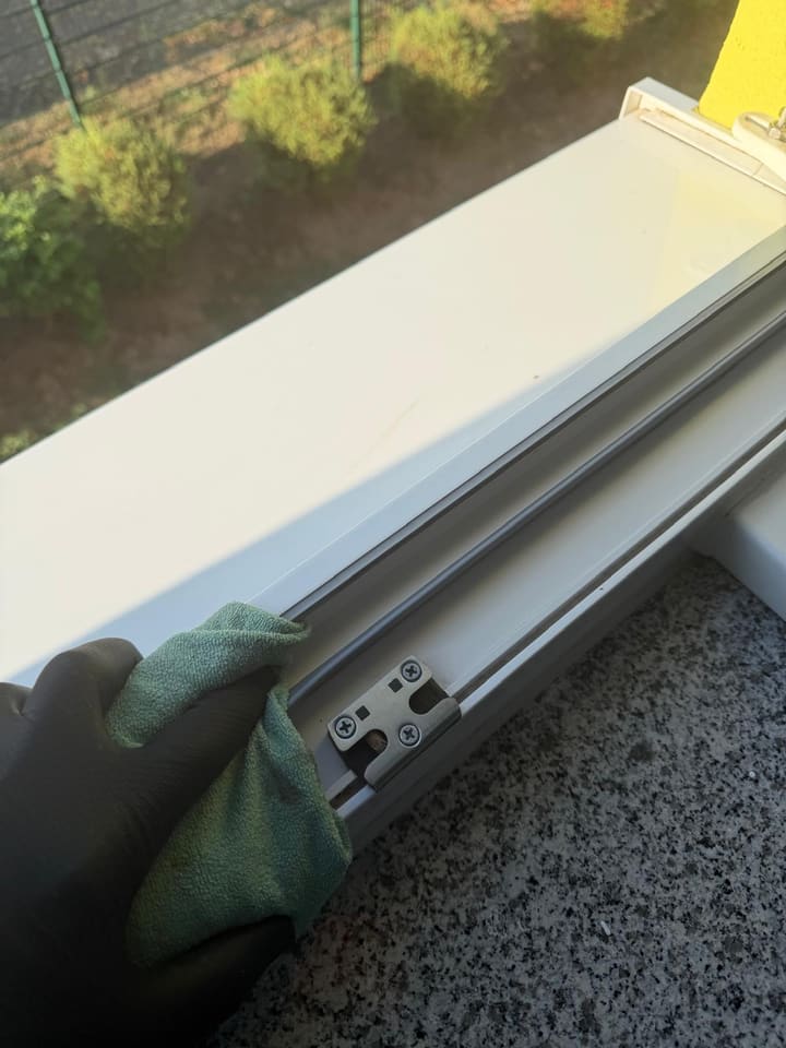 Handschuh und Mikrofasertuch beim Auswischen der Rahmenfalz eines Fensters