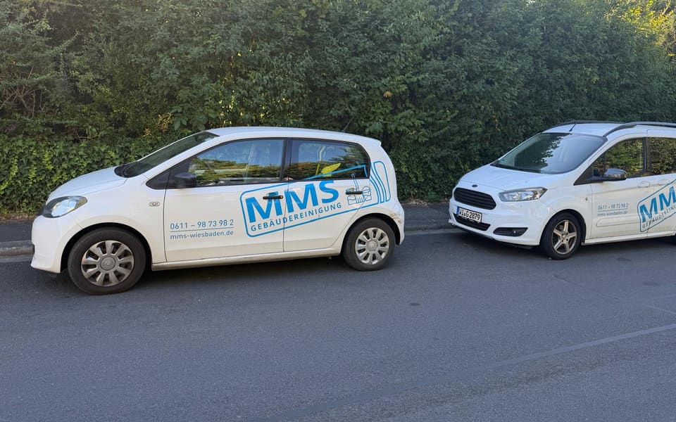 Zwei beschriftete Einsatzfahrzeuge der MMS-Gebäudereinigung am Fahrbahnrand