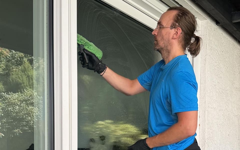 Mitarbeiter wäscht eine bodentiefe Glasfront mit dem Einwascher vor